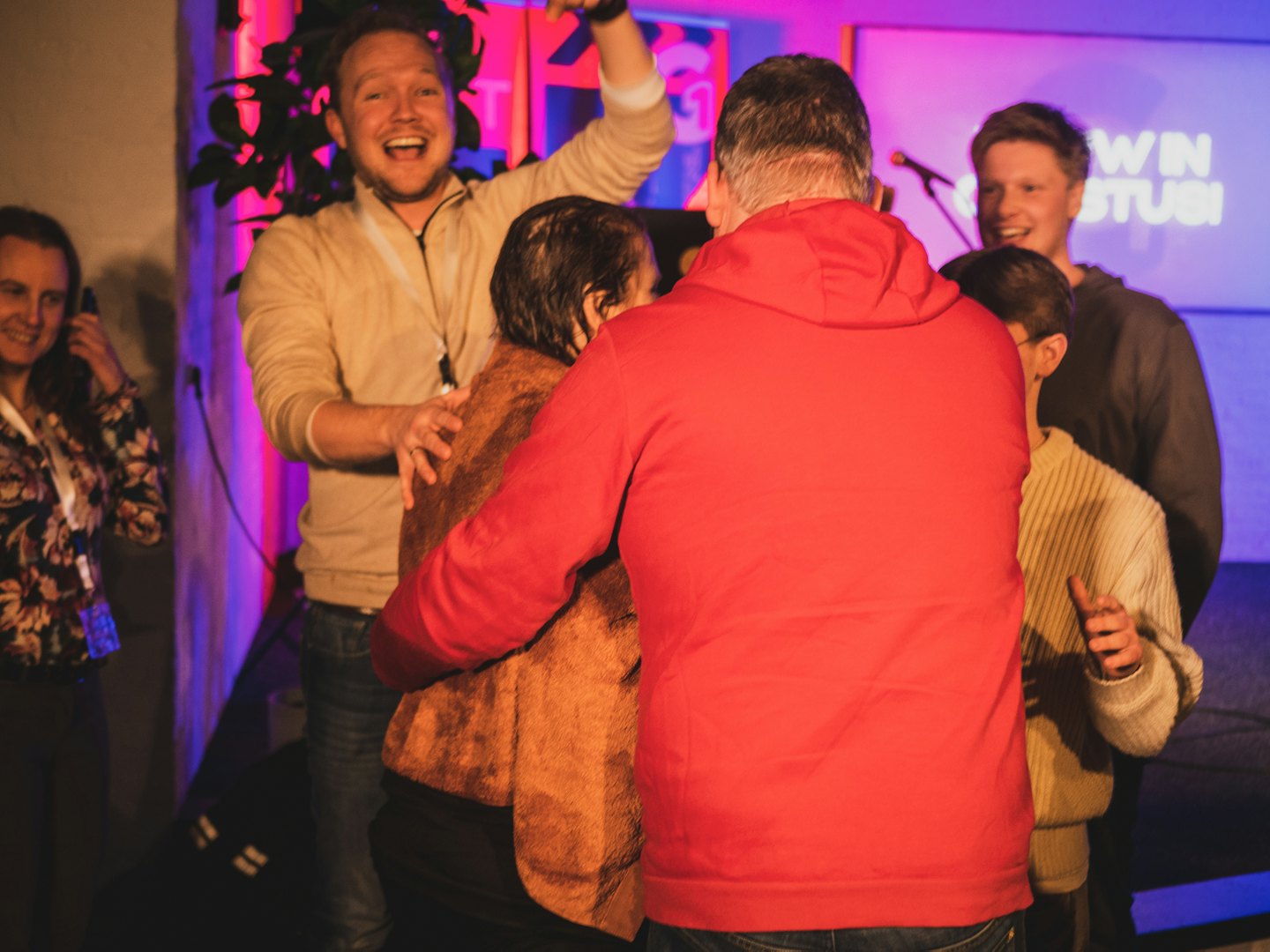 Diverse people celebrating at an indoor event with colorful lighting.